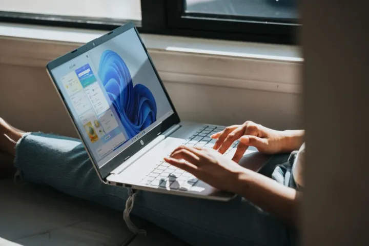 Osoba používá na svém kameni vedle okna laptop Windows 11.
