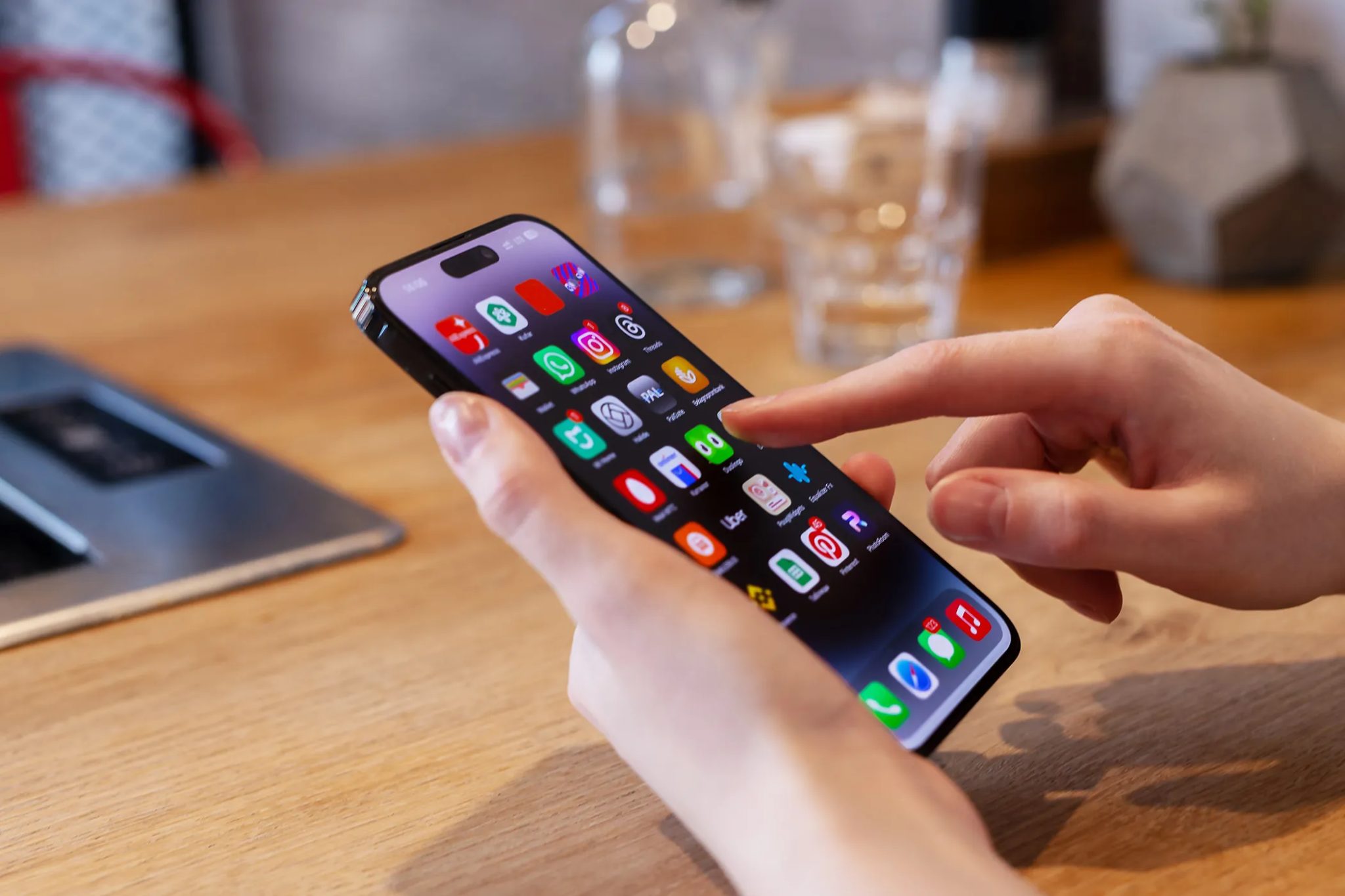 Osoba používá iPhone na stole se skleněným šálkem za ním.