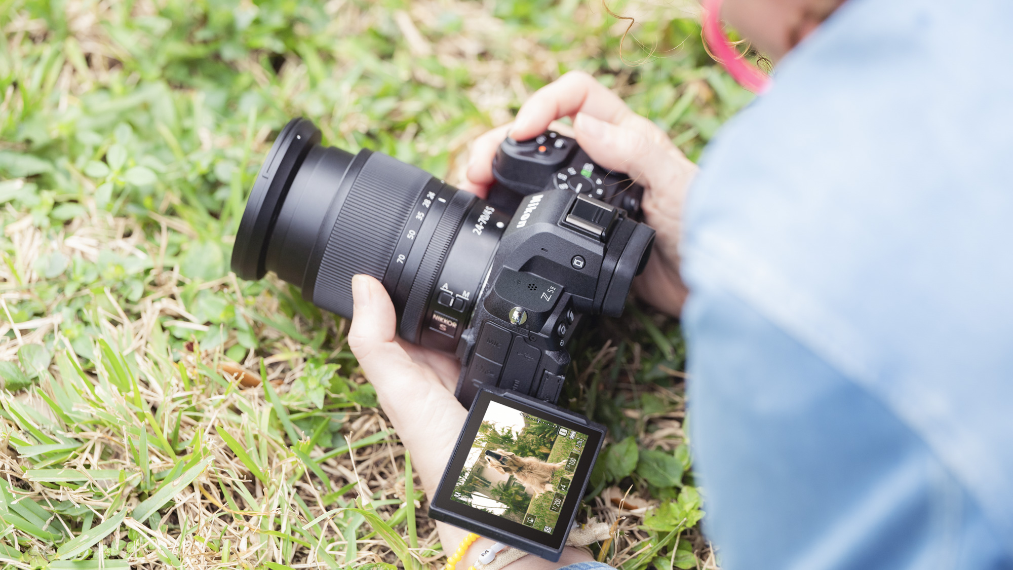Nikon Z5 II v ruce na úrovni země, dotyková obrazovka je otevřená a nahoře